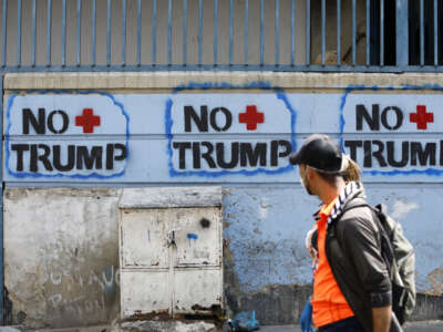 A couple walks past graffiti against U.S. President Donald Trump on March 26, 2020, in Caracas, Venezuela.